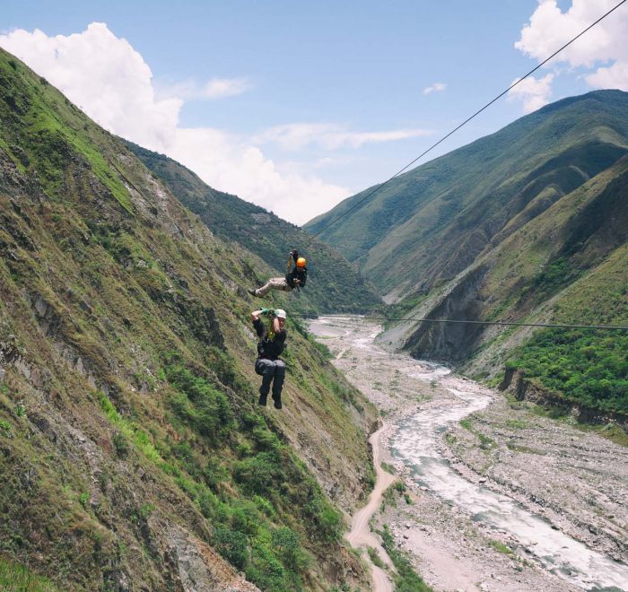 Tourists riding a long zipline high across a deep river valley canyon in Santa Teresa Cusco
