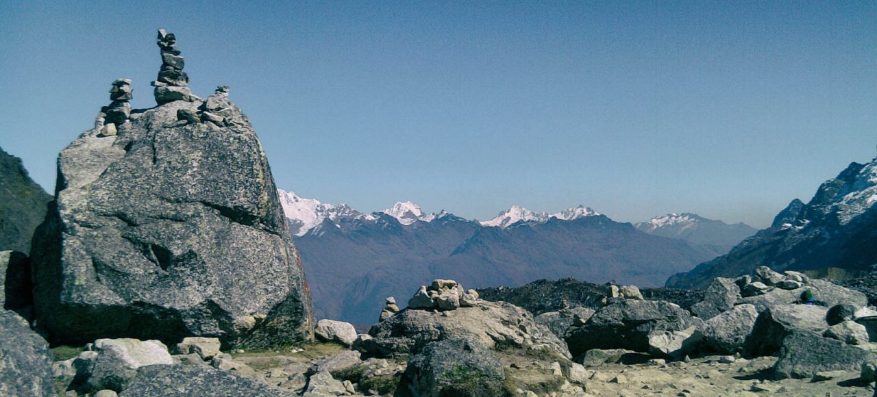 Salkantay Pass sign and rock apacheta pile with the massive snow glacier peak in the background