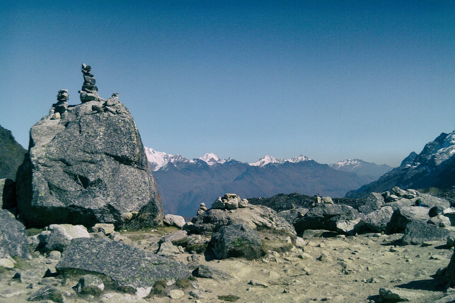 Salkantay Pass sign and rock apacheta pile with the massive snow glacier peak in the background