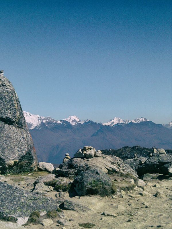 Salkantay Pass sign and rock apacheta pile with the massive snow glacier peak in the background