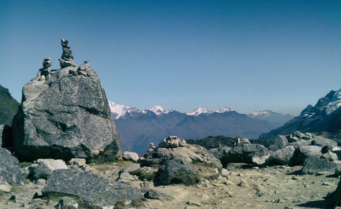 Salkantay Pass sign and rock apacheta pile with the massive snow glacier peak in the background