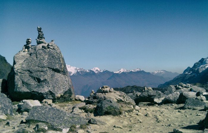 Salkantay Pass sign and rock apacheta pile with the massive snow glacier peak in the background