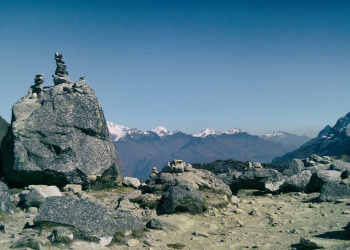 Salkantay Pass sign and rock apacheta pile with the massive snow glacier peak in the background