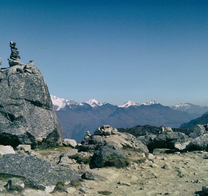 Salkantay Pass sign and rock apacheta pile with the massive snow glacier peak in the background