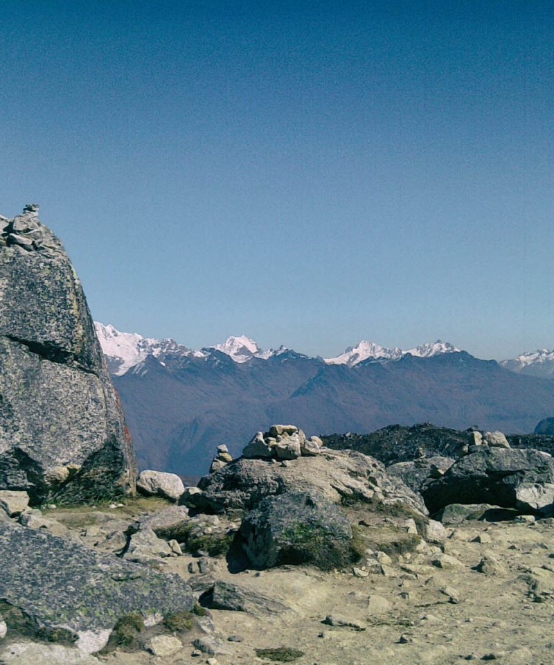 Salkantay Pass sign and rock apacheta pile with the massive snow glacier peak in the background