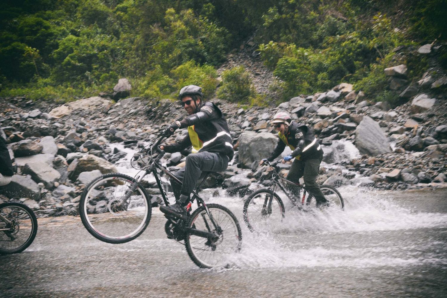 Active mountain bikers splashing through a cold mountain stream during the Inka Jungle Trek