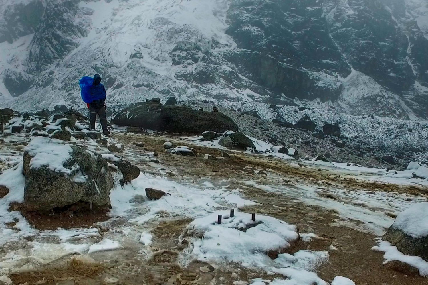 Trekkers climbing the steep rocky trail of the Salkantay Pass with glacier peaks behind them