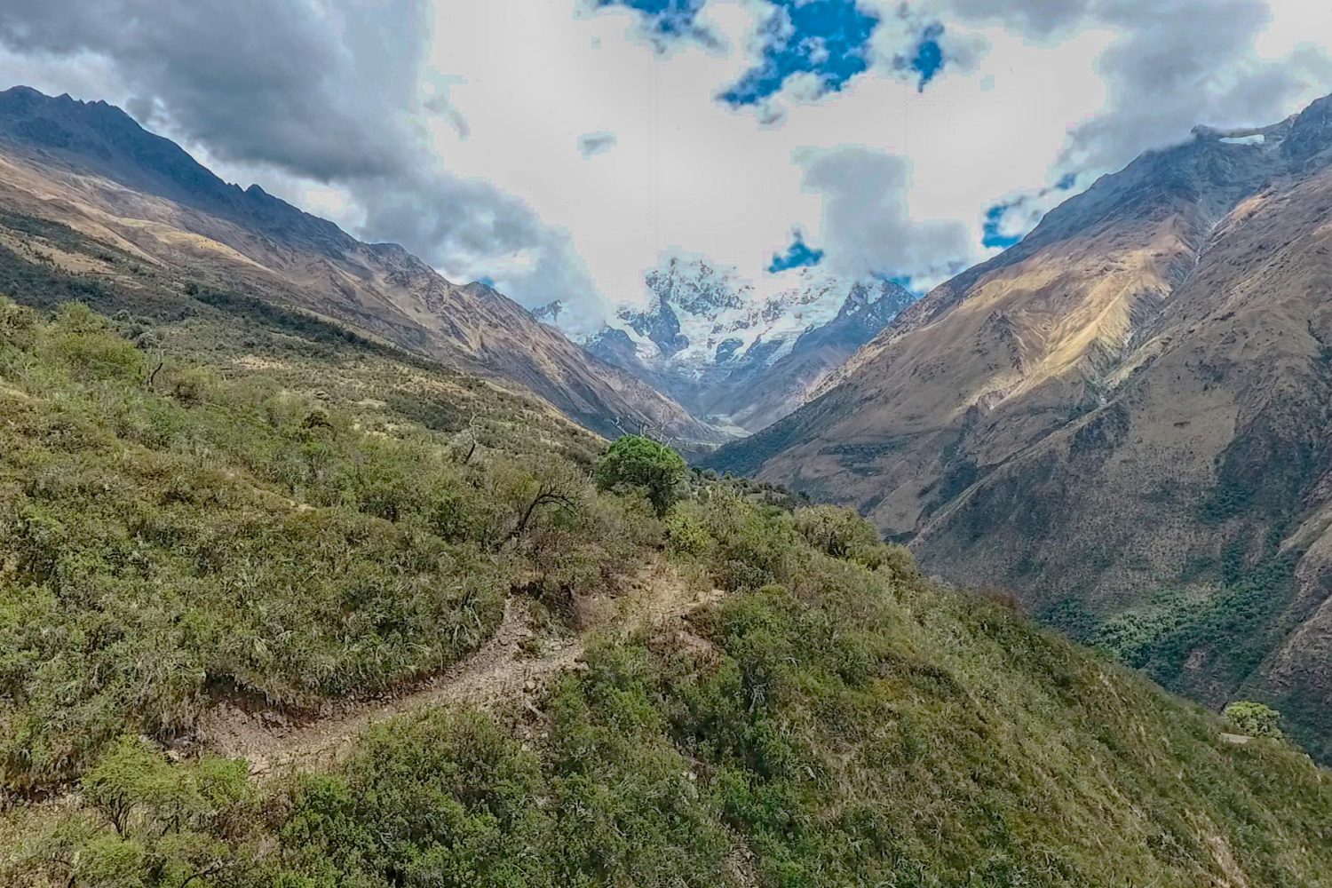 Trekkers walking along a wide mountain plain below the towering glaciers of Salkantay mountain