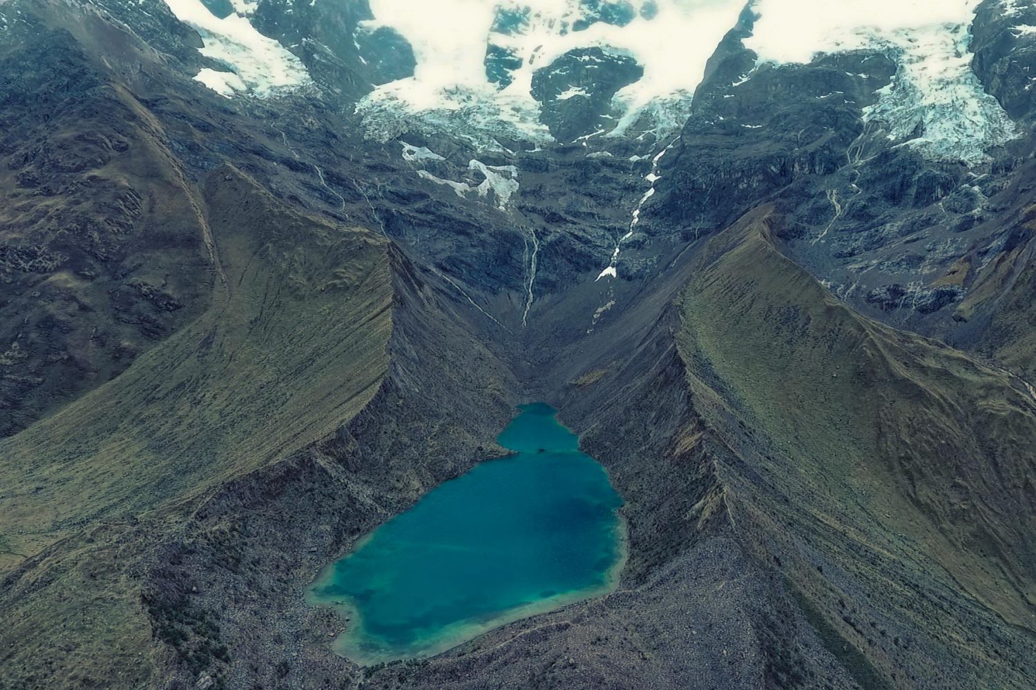 Turquoise waters of Humantay Lake surrounded by dramatic snow glacier peaks on the Salkantay Trek