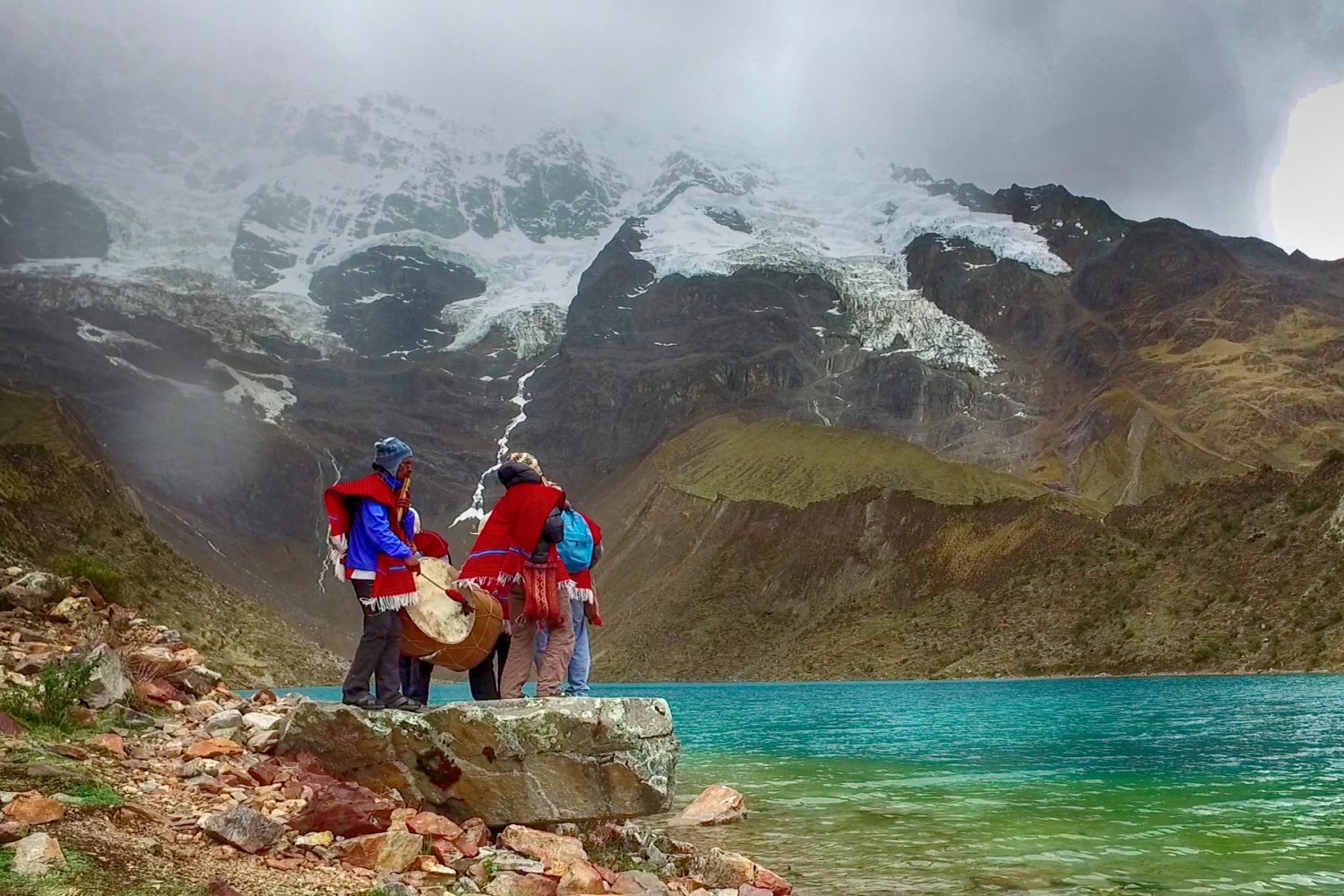 Hikers walking towards the shore of the turquoise Humantay Lake on a sunny day in Cusco