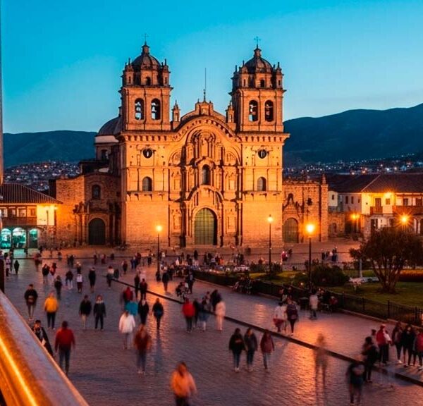 Vista nocturna de la Plaza de Armas iluminada, reflejando la animada vida nocturna en Cusco con gente paseando y luces cálidas de los balcones.
