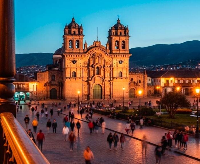 Vista nocturna de la Plaza de Armas iluminada, reflejando la animada vida nocturna en Cusco con gente paseando y luces cálidas de los balcones.
