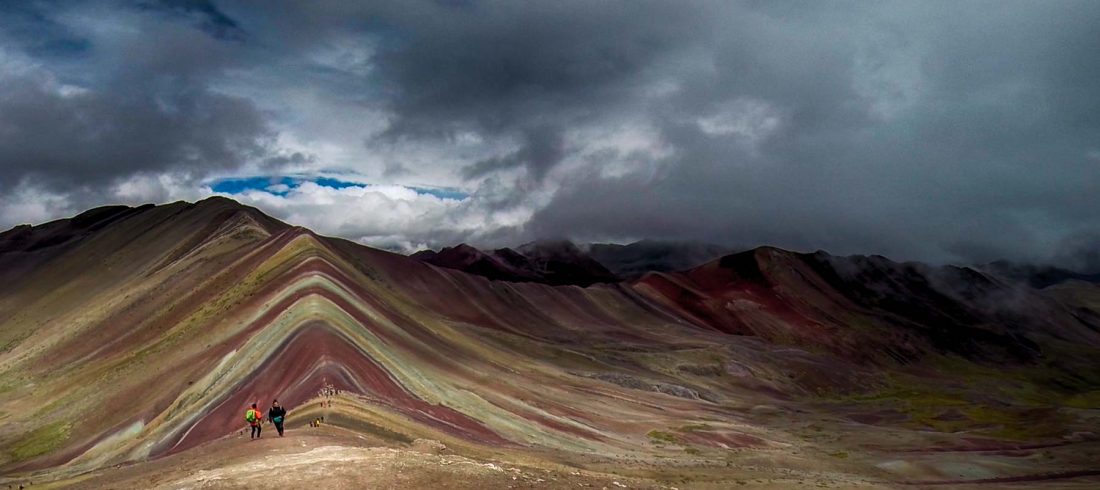 A breathtaking view of Vinicunca, Peru’s iconic Rainbow Mountain near Cusco, featuring vibrant natural stripes of red, yellow, and turquoise under a clear Andean sky.
