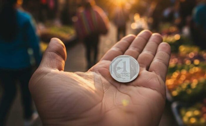 Una mano sosteniendo una moneda de un sol peruano, con un puesto de comida callejera desenfocado en el fondo, ilustrando qué comprar con un sol peruano en Cusco.