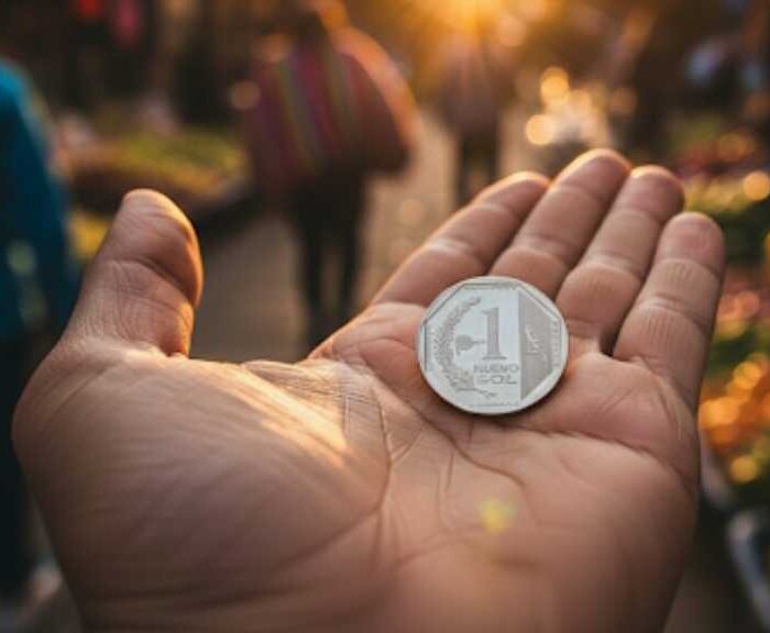 Una mano sosteniendo una moneda de un sol peruano, con un puesto de comida callejera desenfocado en el fondo, ilustrando qué comprar con un sol peruano en Cusco.