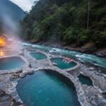 Las paradisíacas Aguas Termales de Cocalmayo al atardecer, con vapor elevándose de las pozas cristalinas junto al río, siendo disfrutadas por viajeros del Inka Jungle