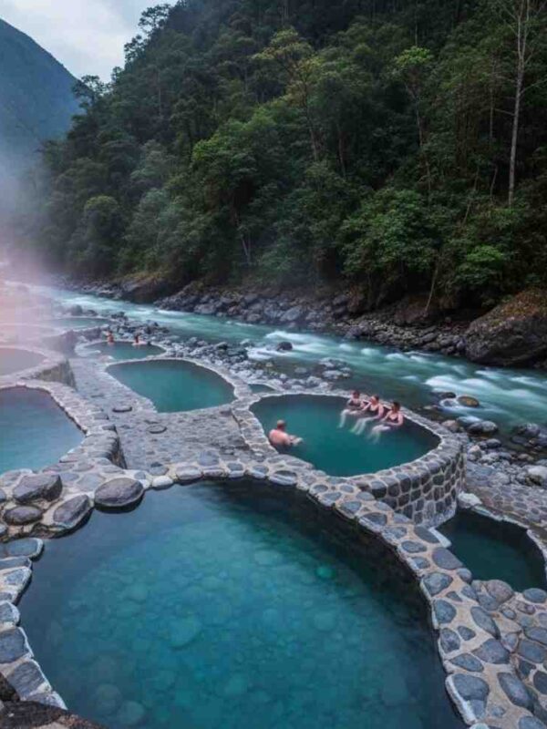 Las paradisíacas Aguas Termales de Cocalmayo al atardecer, con vapor elevándose de las pozas cristalinas junto al río, siendo disfrutadas por viajeros del Inka Jungle