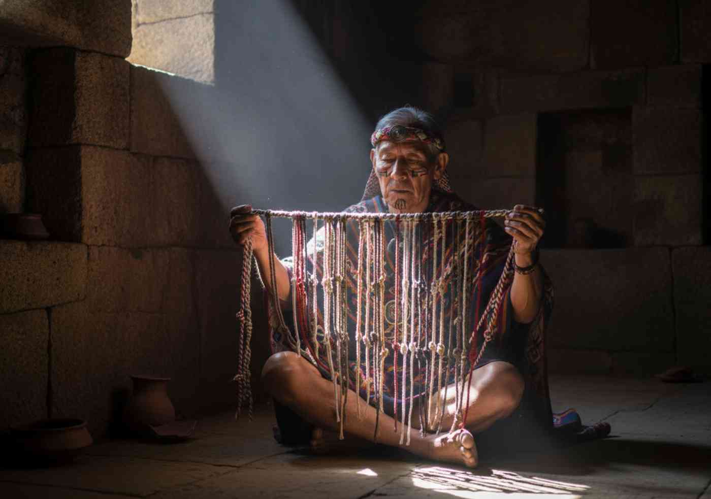 Un sabio Quipucamayoc en una cámara de piedra iluminada por un rayo de sol, examinando el código secreto de los quipus, la escritura perdida del Imperio Inca.