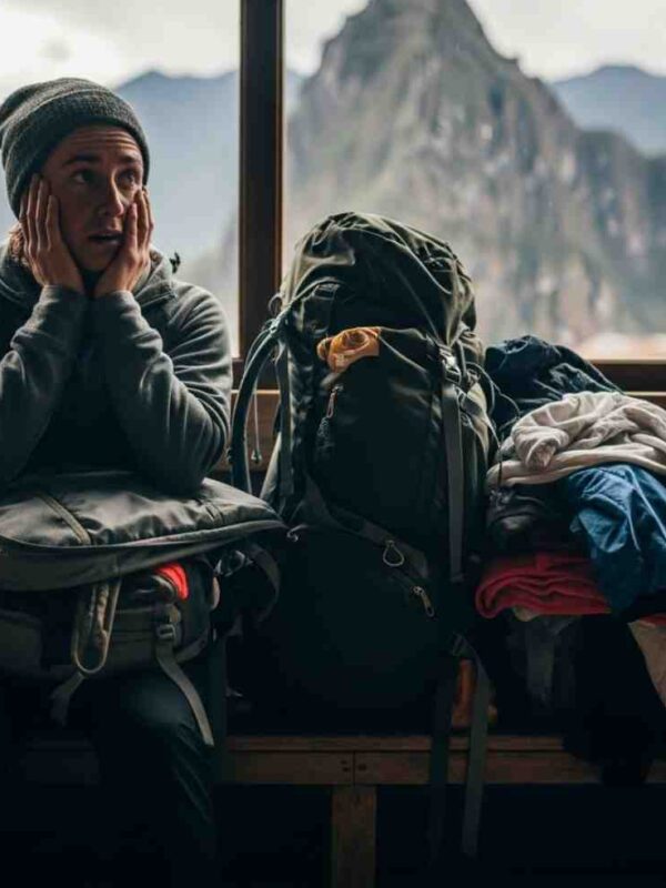 Un trekker revisando su mochila con cara de preocupación frente a una imponente montaña del Salkantay Trek, ilustrando los errores de equipaje