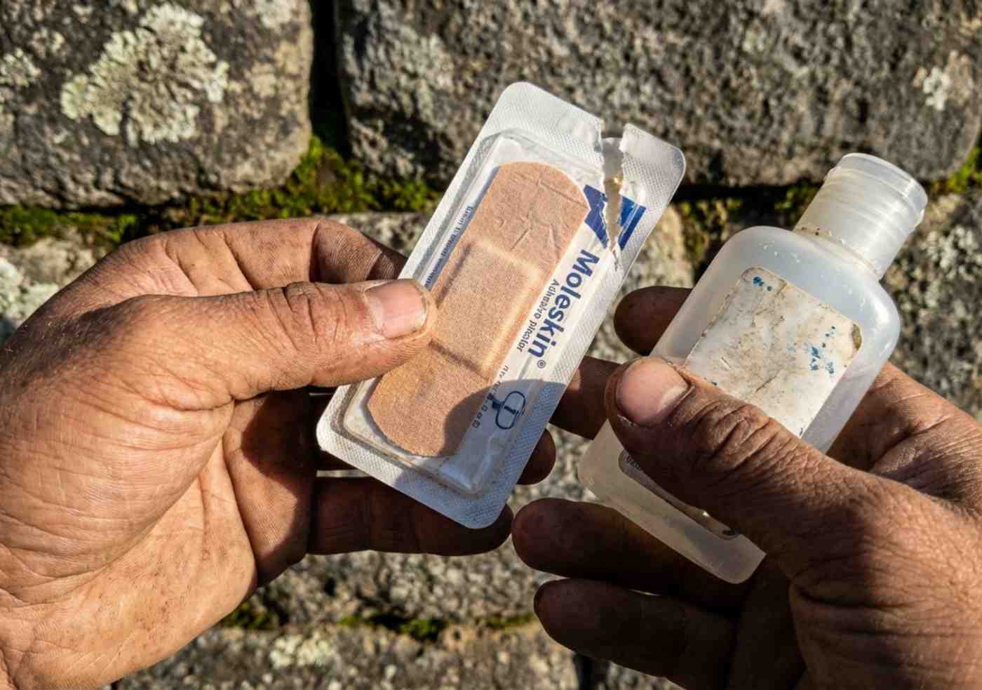 Manos sucias de tierra sosteniendo un parche para ampollas y gel desinfectante sobre una roca