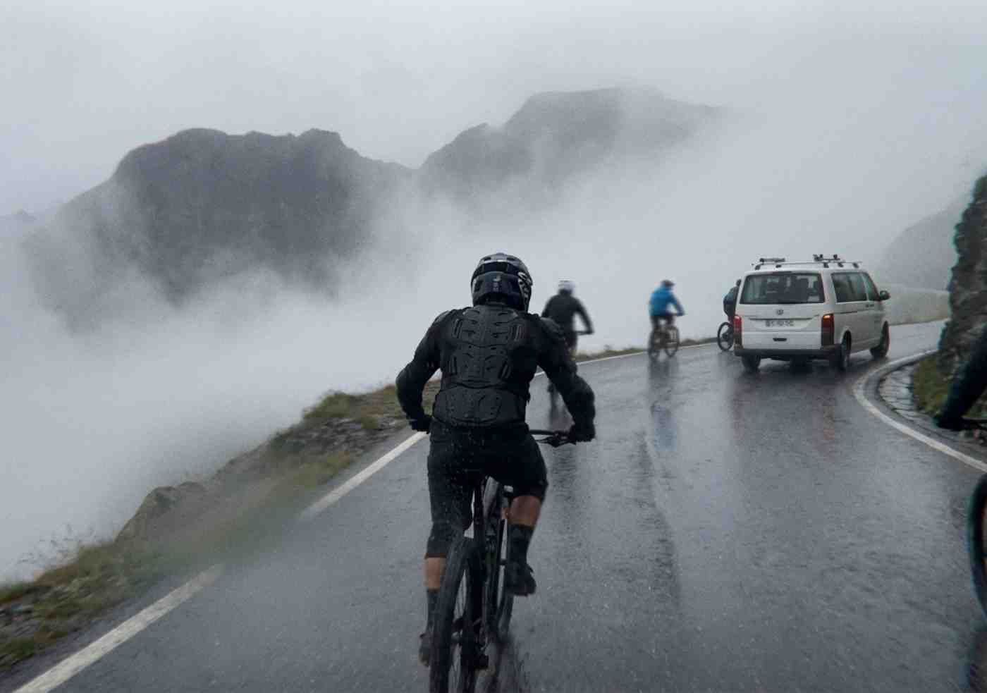 Vista en primera persona (o casi) de un ciclista con casco integral descendiendo por una carretera asfaltada mojada y con niebla en el tramo de bicicleta del Inca Jungle.