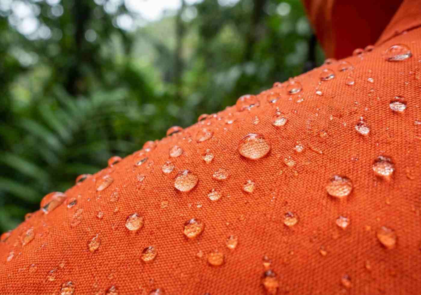 Primer plano de gotas de agua sobre una casaca cortavientos de nylon naranja