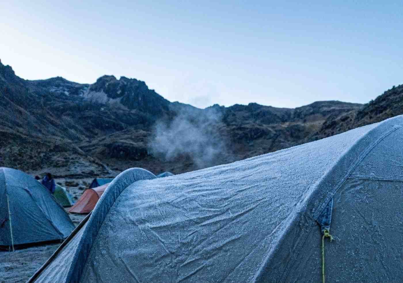 Primer plano de una carpa de campaña cubierta por una fina capa de escarcha blanca al amanecer en un campamento de altura del Camino Inca.