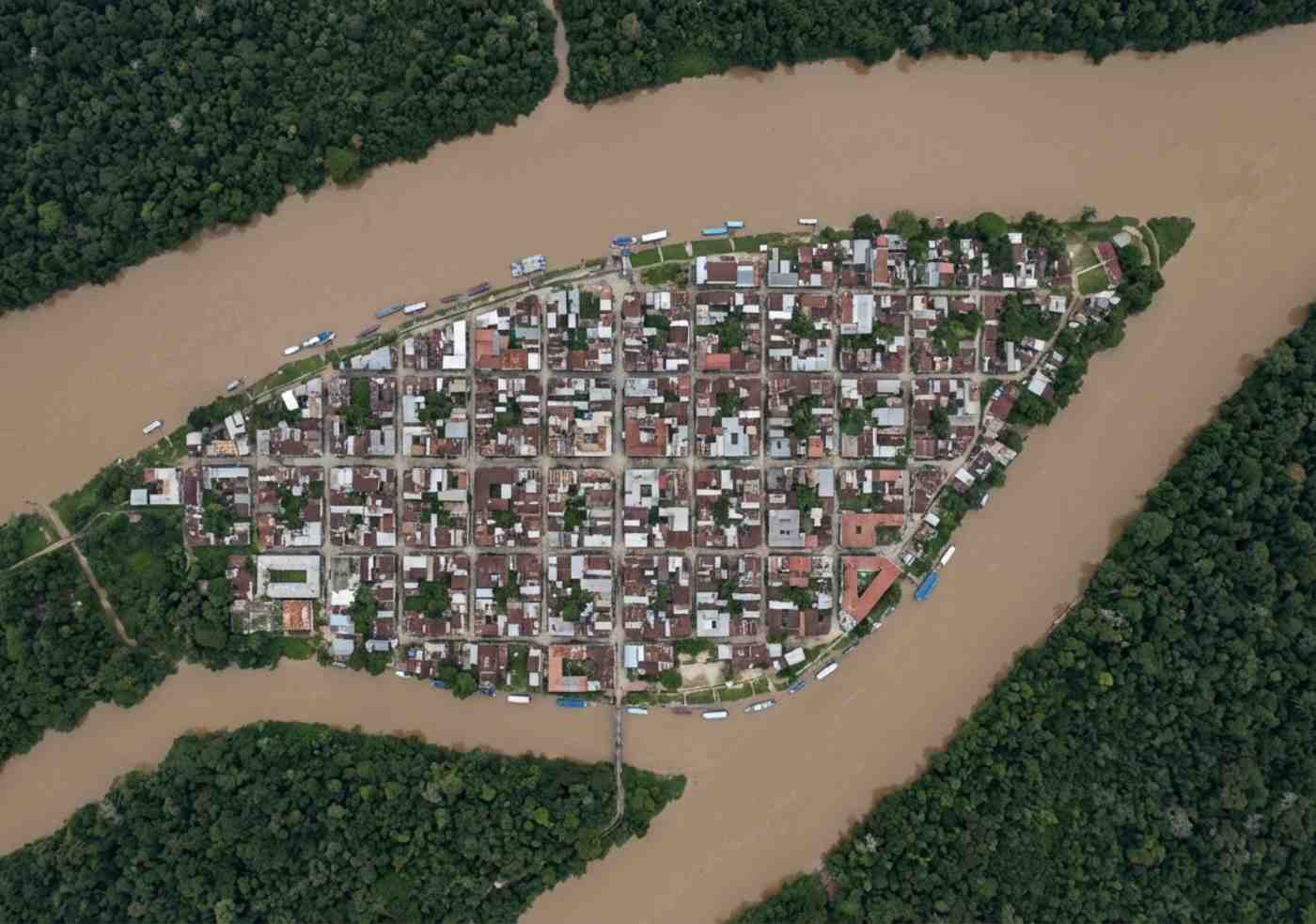 Vista cenital de dron mostrando la ciudad de Iquitos rodeada completamente por agua y selva, sin conexiones viales visibles.