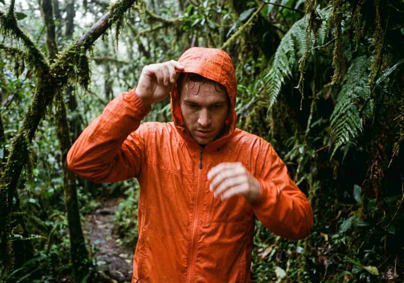 Plano medio de viajero poniéndose un poncho de lluvia sobre casaca polar en medio del bosque nuboso