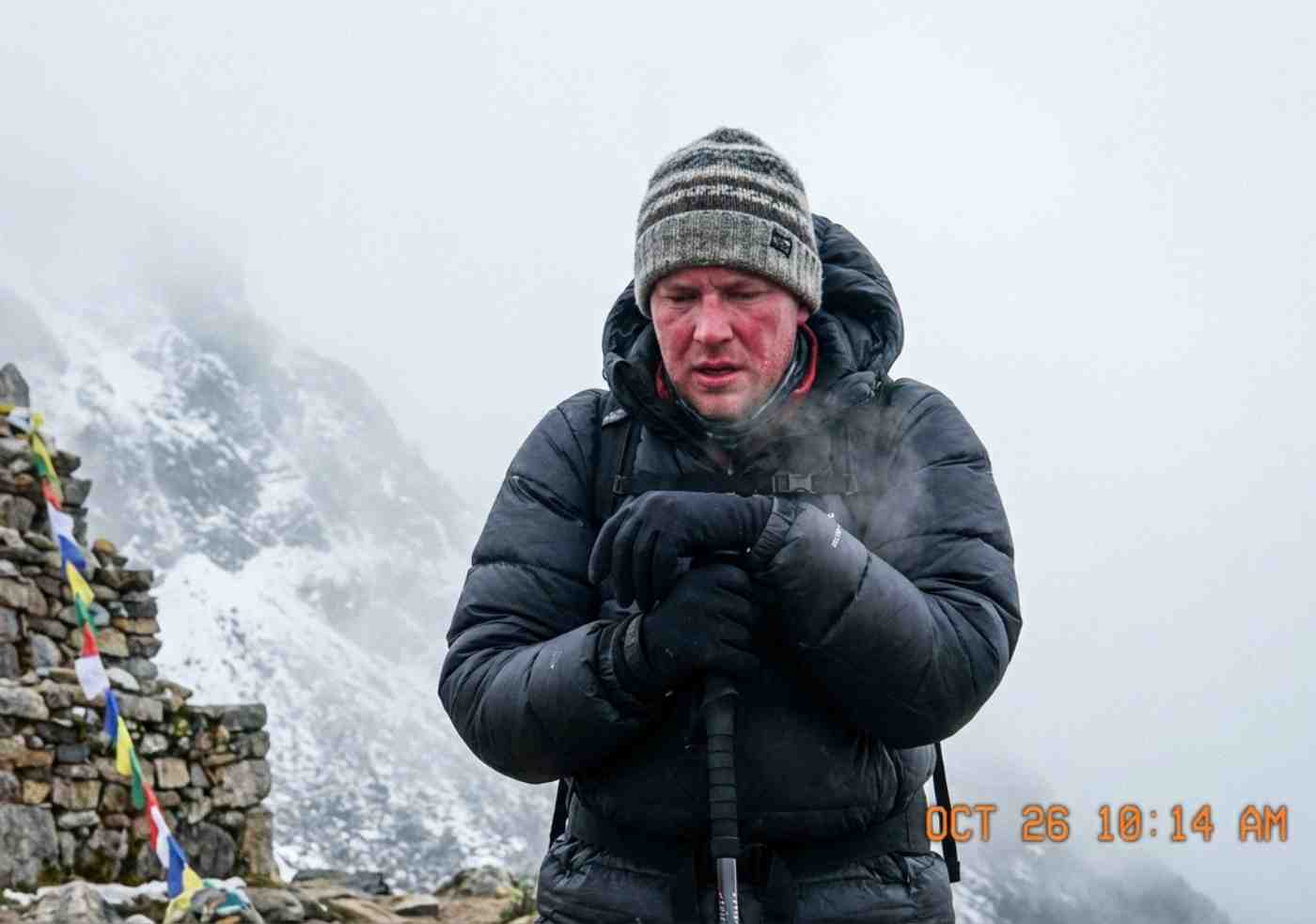 Un excursionista exhausto recuperando el aliento junto a una apacheta de piedras en el paso Salkantay a 4630 metros de altura, con niebla y frío