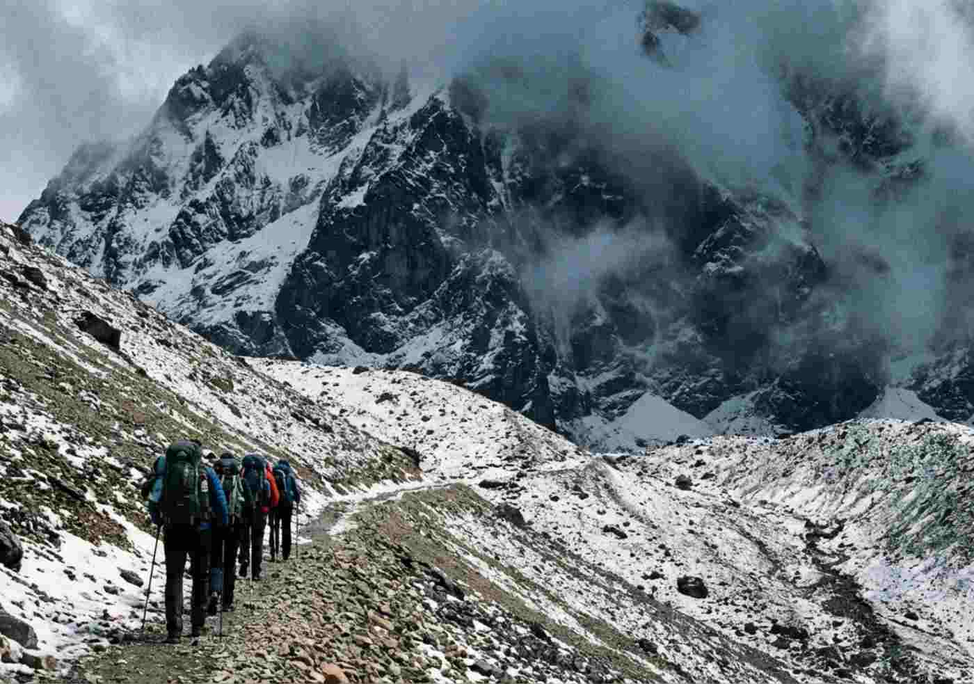 Un grupo pequeño de excursionistas con mochilas grandes camina con esfuerzo por un sendero empinado y rocoso hacia un paso de montaña alto y nublado en los Andes peruanos, mostrando la dificultad física del ascenso.