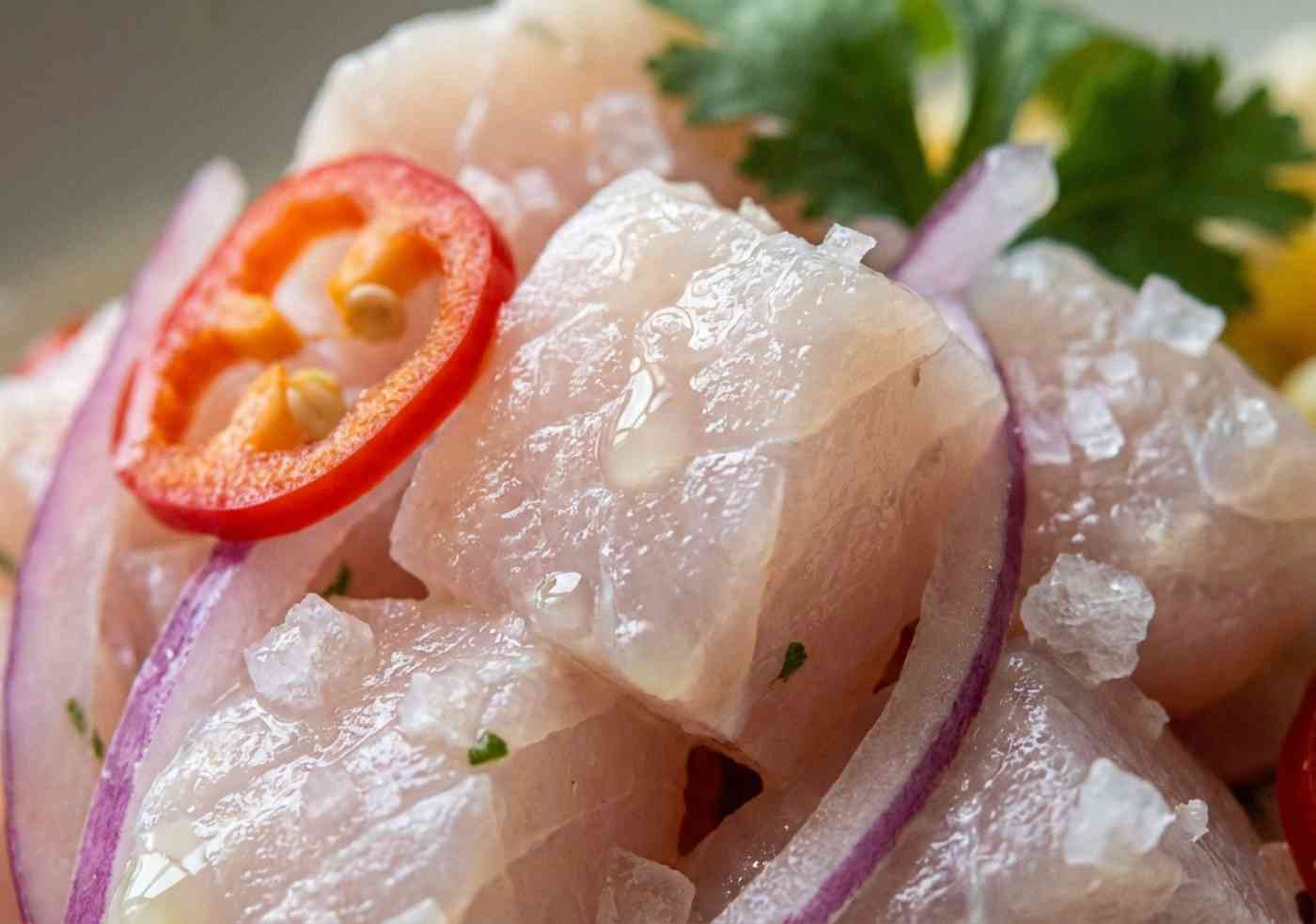 Macro de trozos de pescado blanco fresco con ají limo, cebolla roja y gotas de limón piurano.