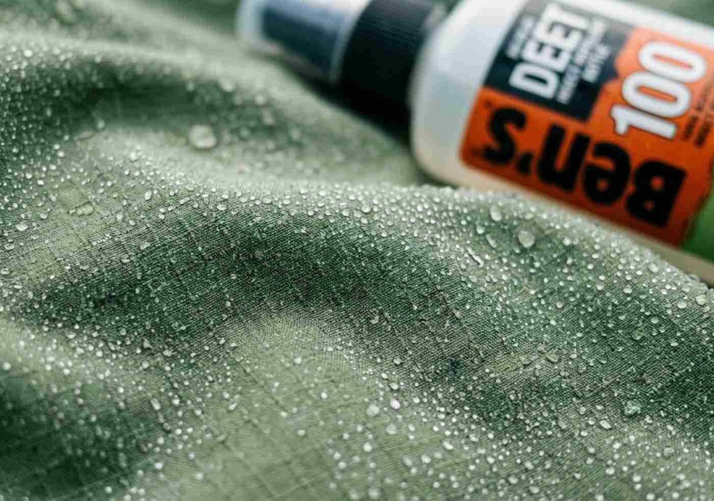 Macro de la textura de una camisa de trekking de secado rápido con gotas de humedad y un repelente de insectos al lado.