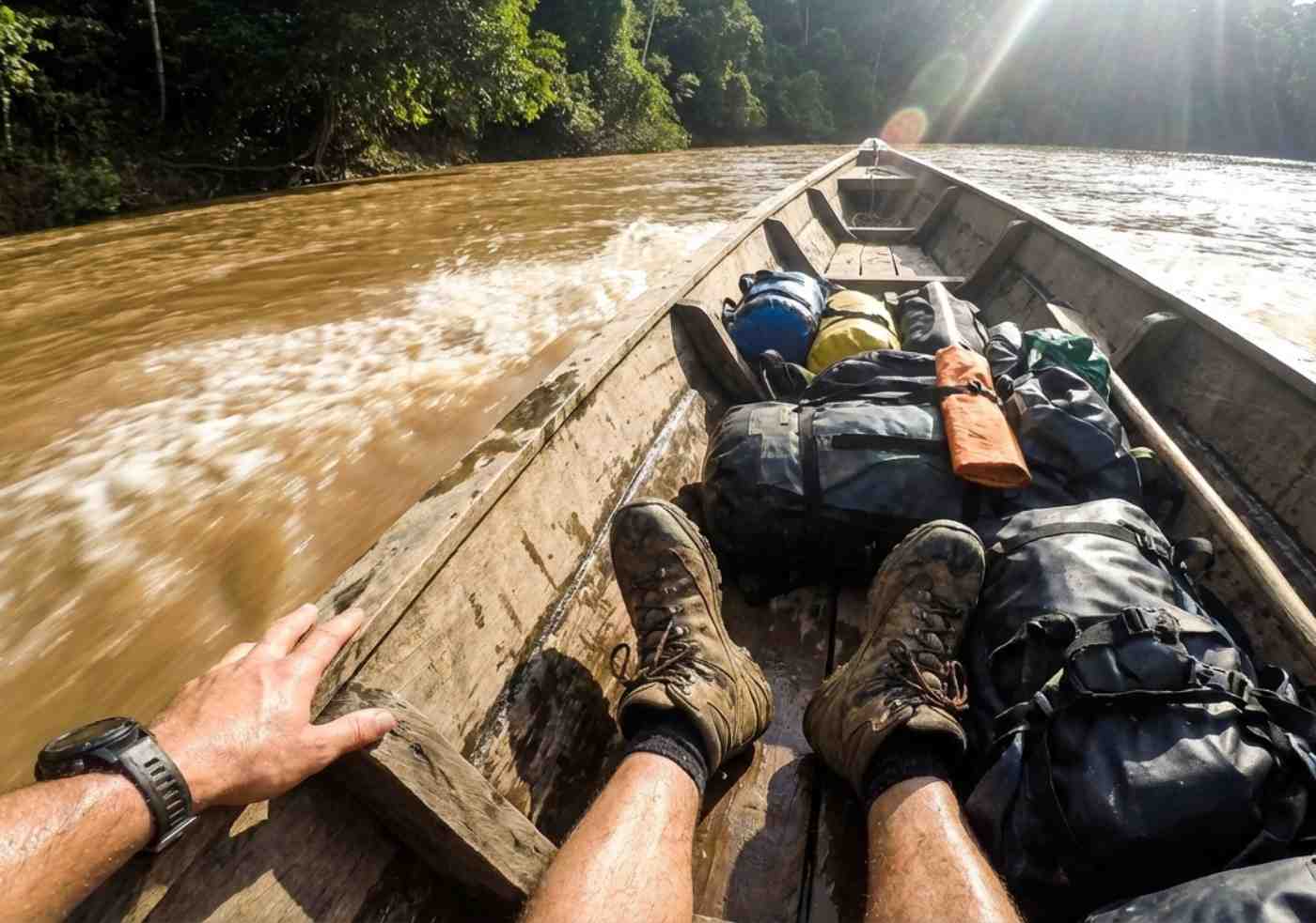 Pasajeros con equipo de expedición navegando en un bote largo de madera por el río Manu