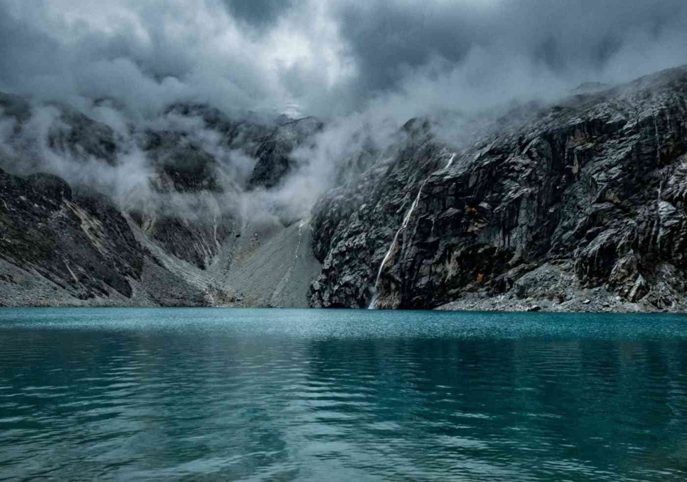 Laguna glaciar turquesa en Huaraz rodeada de niebla y paredes de granito bajo un cielo nublado.