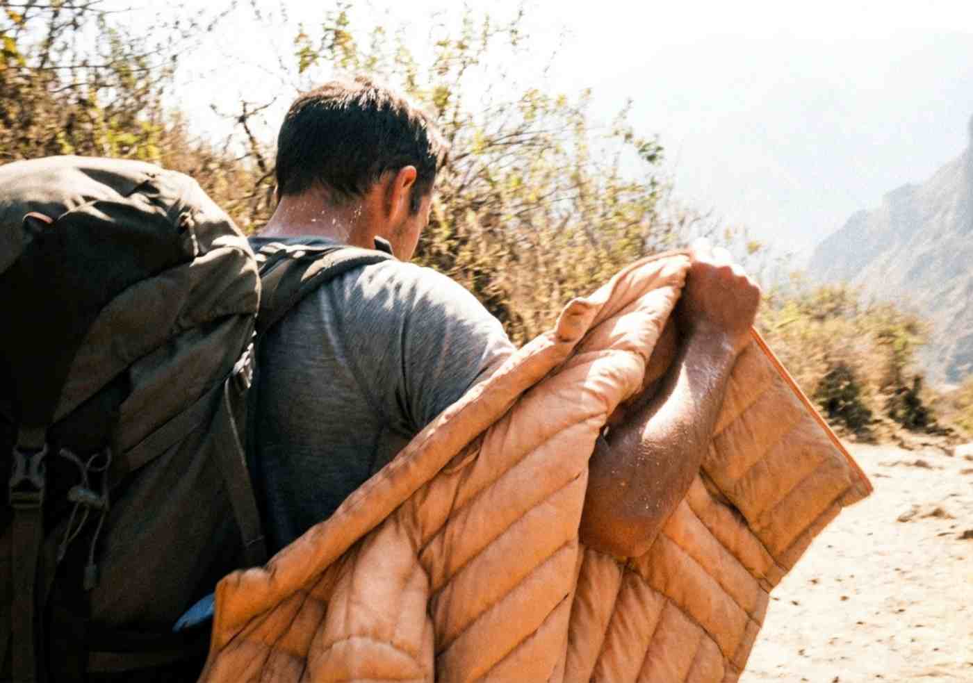 Foto estilo móvil de un senderista sudado de espaldas, quitándose una casaca ligera bajo el sol intenso del cañón del Apurímac.