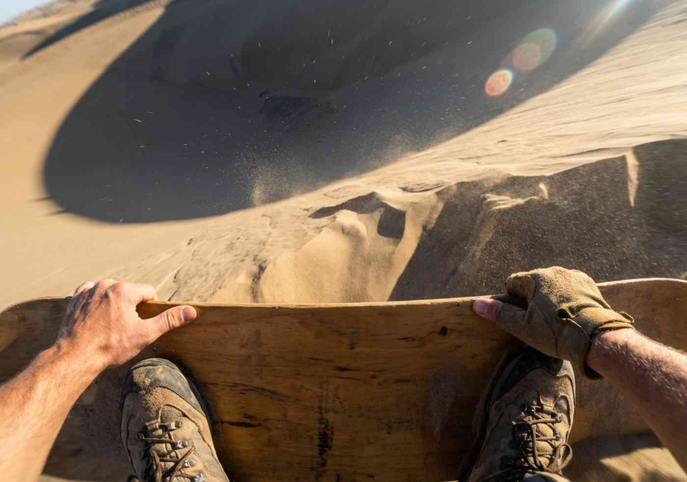 Primer plano desde la perspectiva del viajero sentado en una tabla de sandboarding mirando hacia un descenso empinado en el desierto