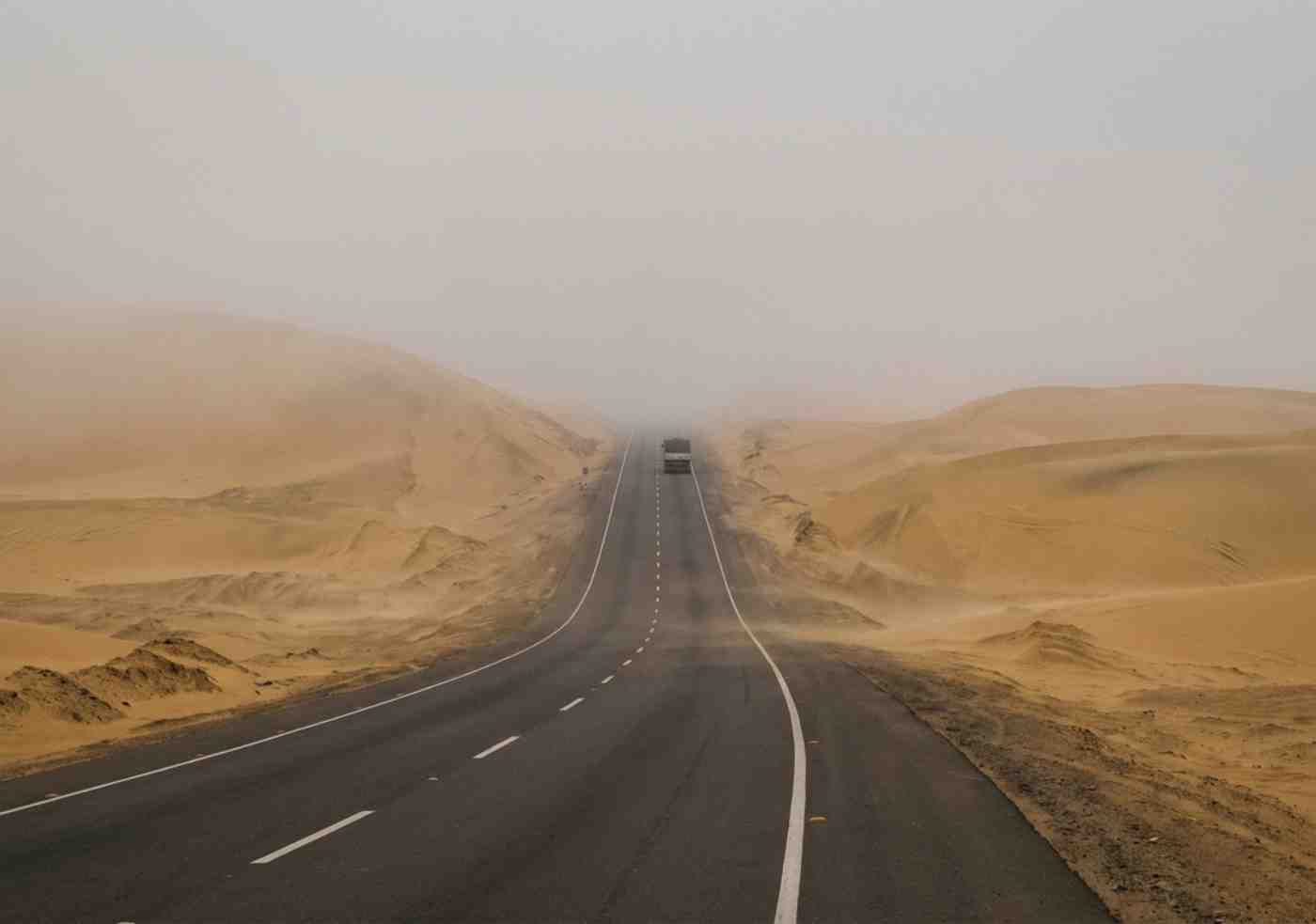 Carretera Panamericana Sur atravesando el desierto peruano con neblina matutina y dunas al fondo.