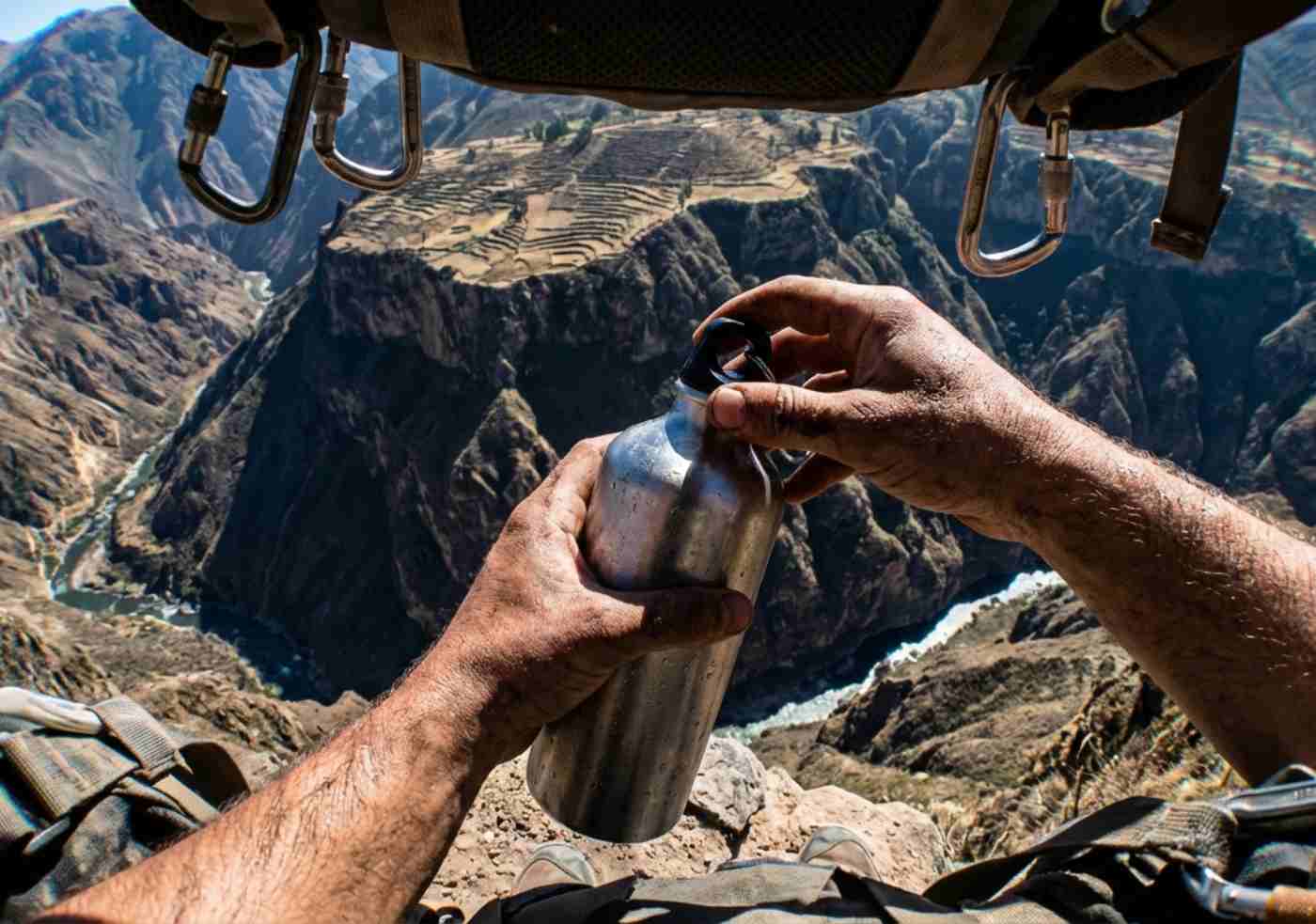 Perspectiva subjetiva (POV) de las manos de un guía sosteniendo un mapa o una botella de agua frente al abismo del Colca.