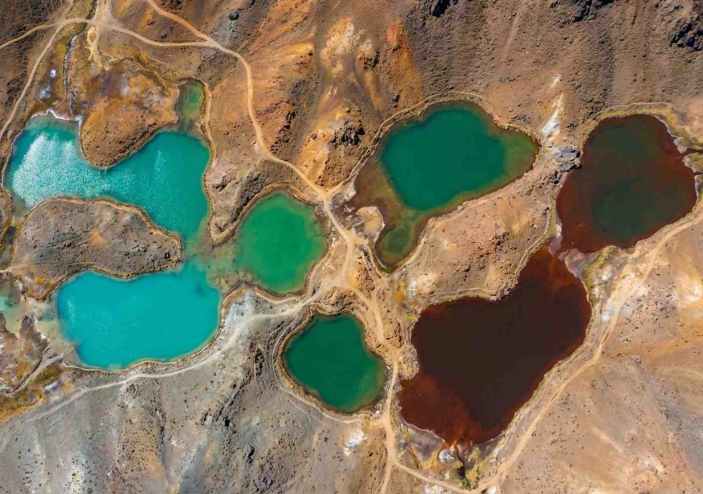 Fotografía con dron mirando hacia abajo a varias lagunas glaciares de colores turquesa y verde brillante rodeadas de paisaje andino árido.